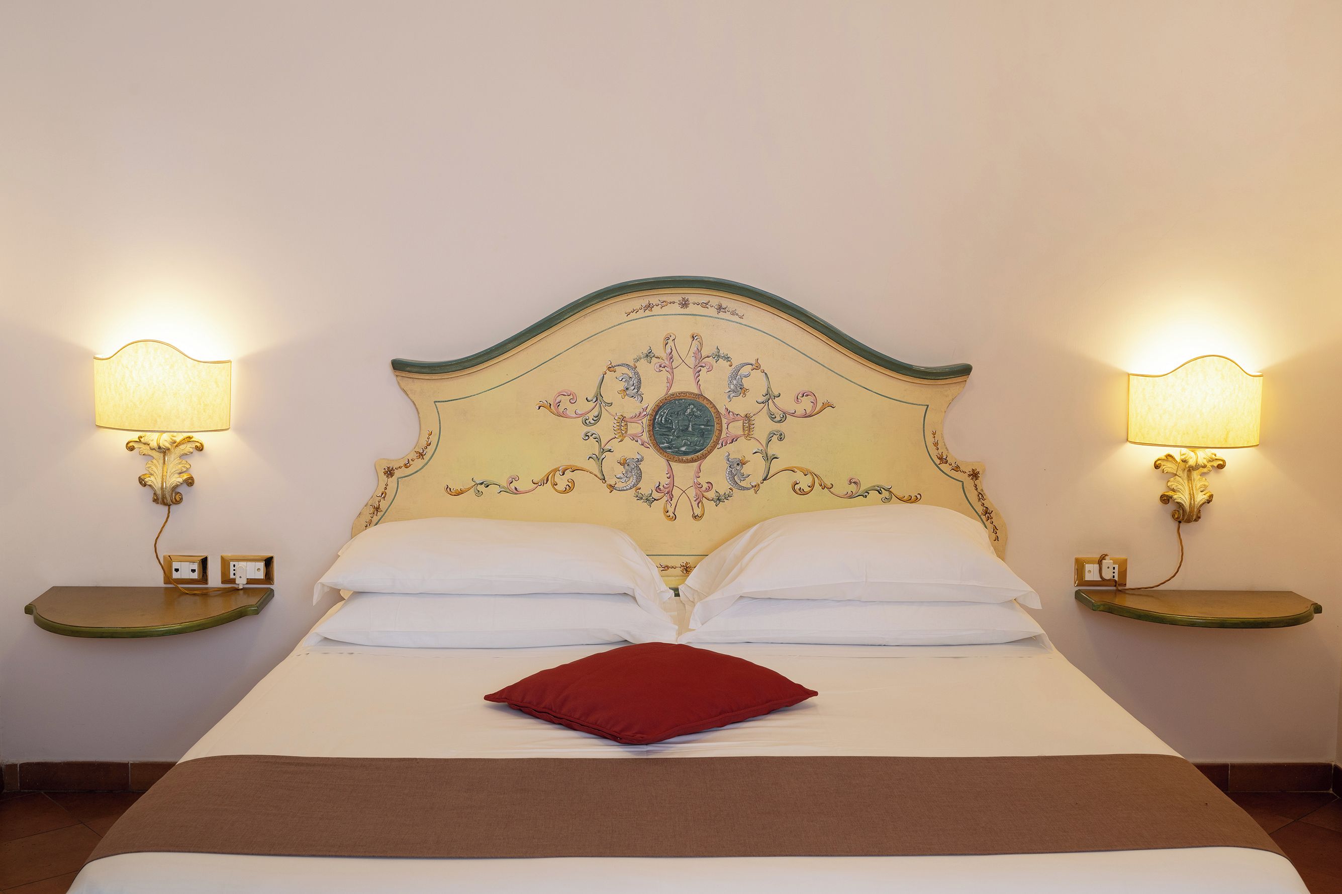 Un lit avec une tête de lit décorative, deux lampes de chevet et un oreiller rouge.