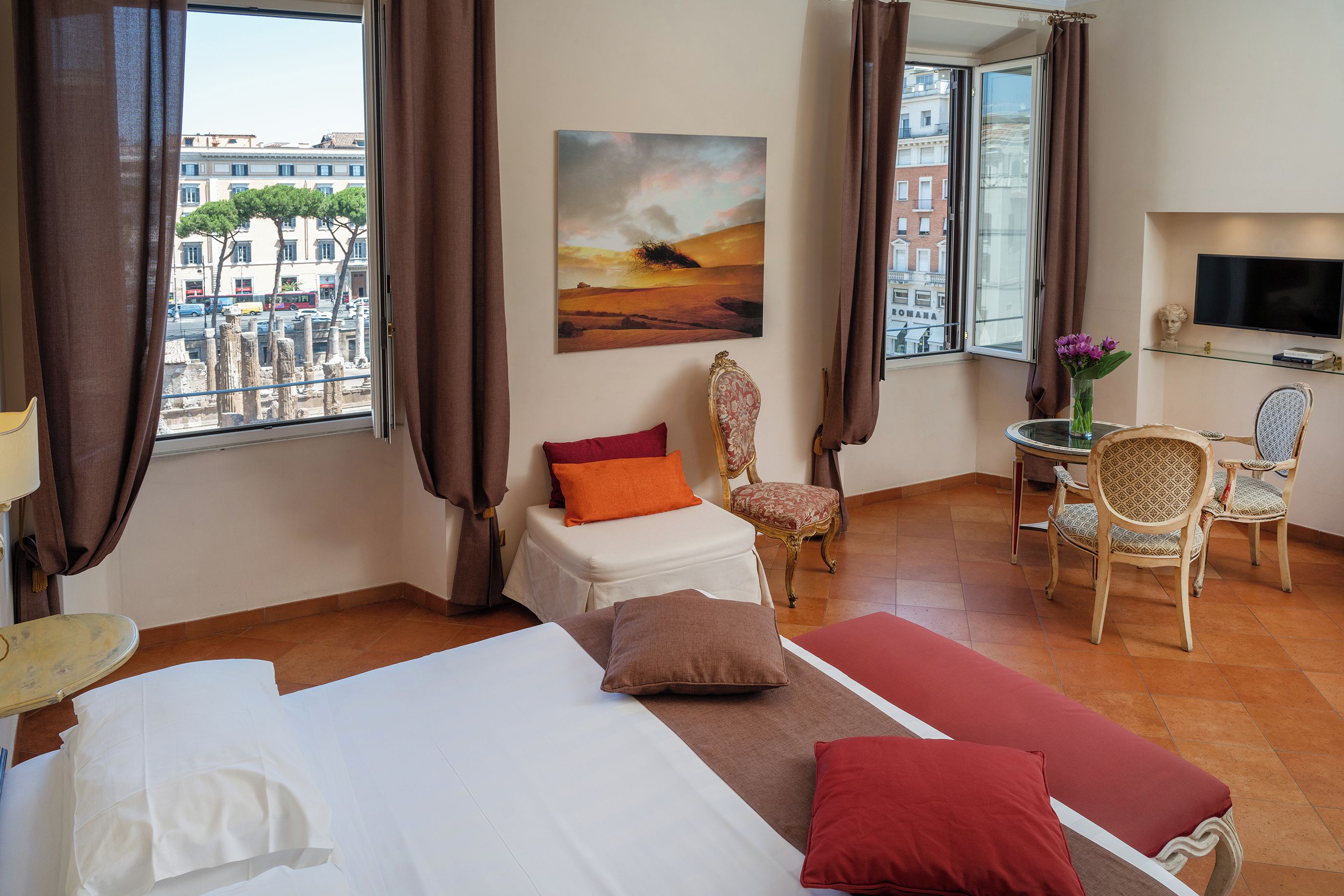 Een hotelkamer met een bed, twee stoelen, een klein tafeltje, een schilderij en een televisie.