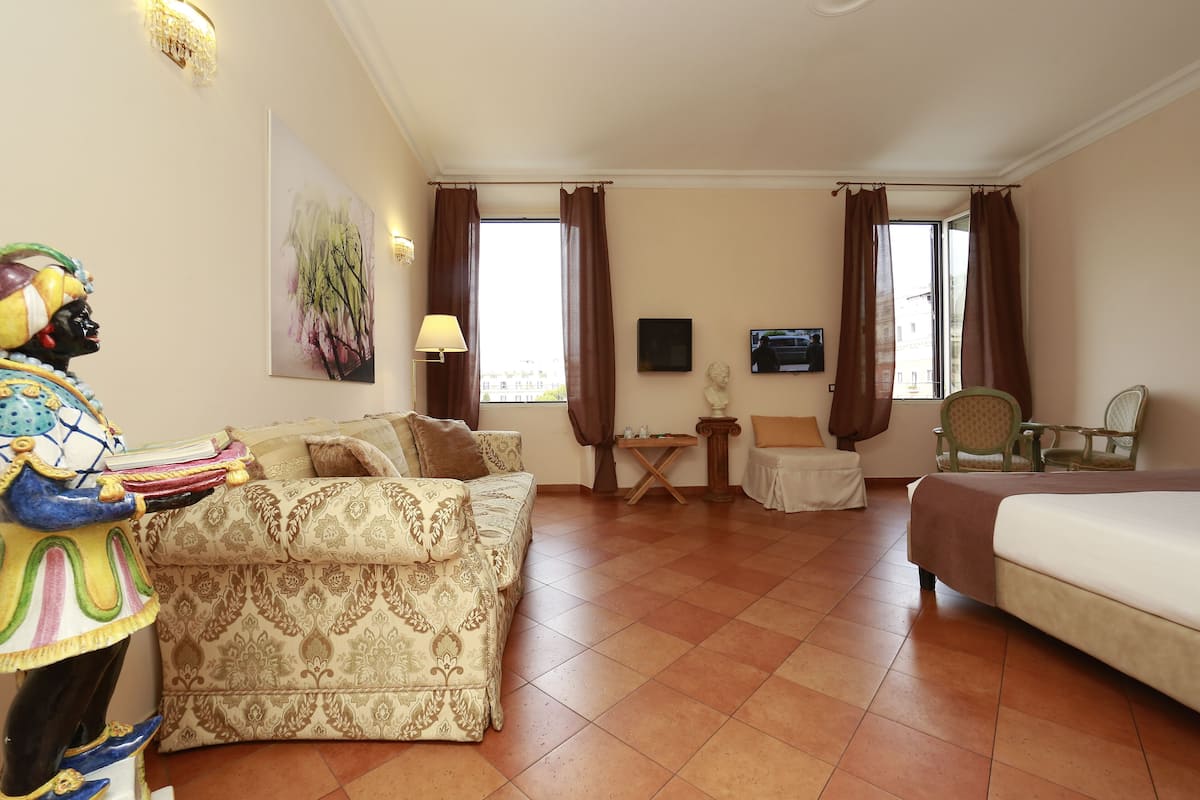 A hotel room with a patterned sofa, a bed, a TV, and a view of the city through large windows.