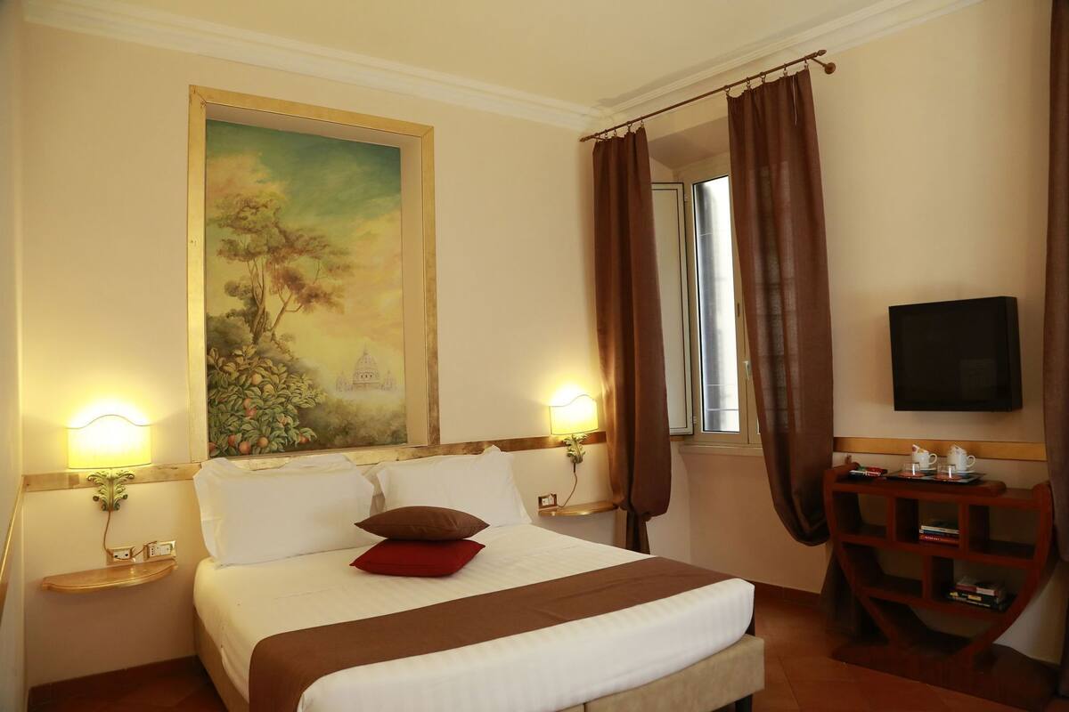 A hotel room with a bed, a painting, a TV, and a small table with a tray.