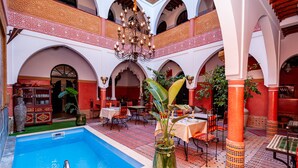 Um pátio com piscina, área de refeições e colunas decorativas.