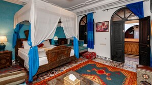 Quarto tradicional com cama de dossel, cabeceira de madeira e carpete estampado.