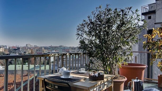 Terraza en la azotea con una mesa lista para el desayuno, una planta en maceta y vistas de la ciudad.