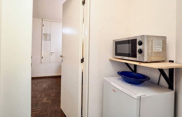 A compact kitchen with a microwave on a shelf, a small refrigerator, and a blue bowl on top.