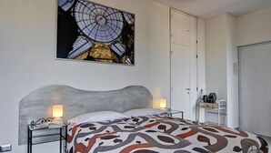 Un dormitorio con una cama, mesitas de noche, un escritorio y un cuadro grande del interior de un edificio.