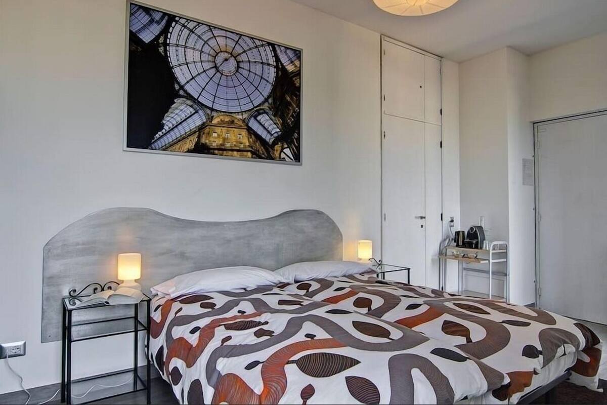 Un dormitorio con una cama, mesitas de noche, un escritorio y un cuadro grande del interior de un edificio.