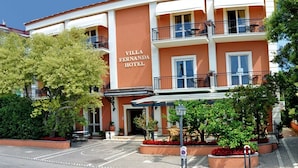 A multi-story building with balconies, a sign reading "Villa Fernanda Hotel," and a paved entrance area with potted plants. - Villa Fernanda (Massa Lubrense)