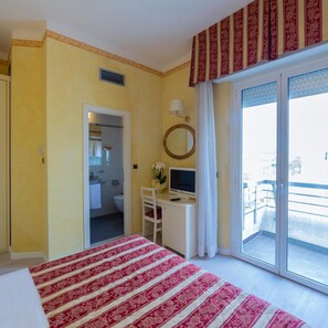 A hotel room with a bed, a desk with a computer, a TV, a bathroom, and a balcony with a view.