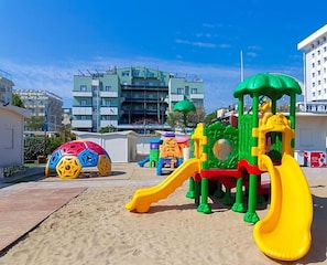 A playground with a slide and climbing structures, set against a backdrop of residential buildings.