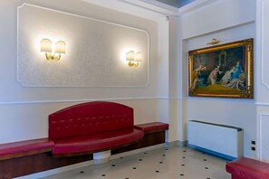 A reception area with a red bench, wall-mounted light fixtures, and a framed painting.