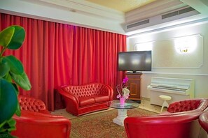 A room with a red sofa, a television, a piano, and a small stool. - La Fiorita (Rimini)