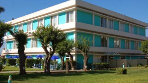 A multi-story hotel with a flat facade, large windows, and a well-maintained lawn with trees and umbrellas. - Mabrouk Hotel and Suites- Adult Only (Agadir)