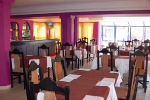 Ein Essbereich mit Tischen und Stühlen, eine Bar mit einer Theke und große Fenster für viel Tageslicht.