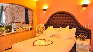 A hotel room with a large bed, a decorative mirror, wall sconces, and a bouquet of flowers. - Mabrouk Hotel and Suites- Adult Only (Agadir)