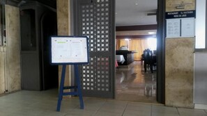A hotel entrance with a reception desk, a blue information stand, and a view into the dining area. - Mabrouk Hotel and Suites- Adult Only (Agadir)
