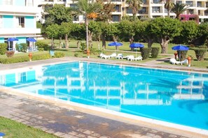 A swimming pool with lounge chairs and umbrellas, surrounded by greenery and a building in the background. - Mabrouk Hotel and Suites- Adult Only (Agadir)