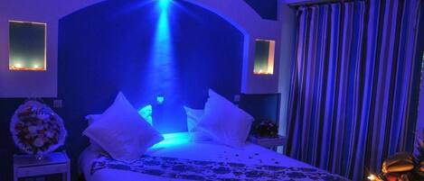 A hotel room with a bed, a nightstand, a vase of flowers, and a curtain.