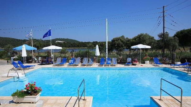 A swimming pool with blue lounge chairs and umbrellas, surrounded by greenery and flags. - Golden Beach (Skiathos)