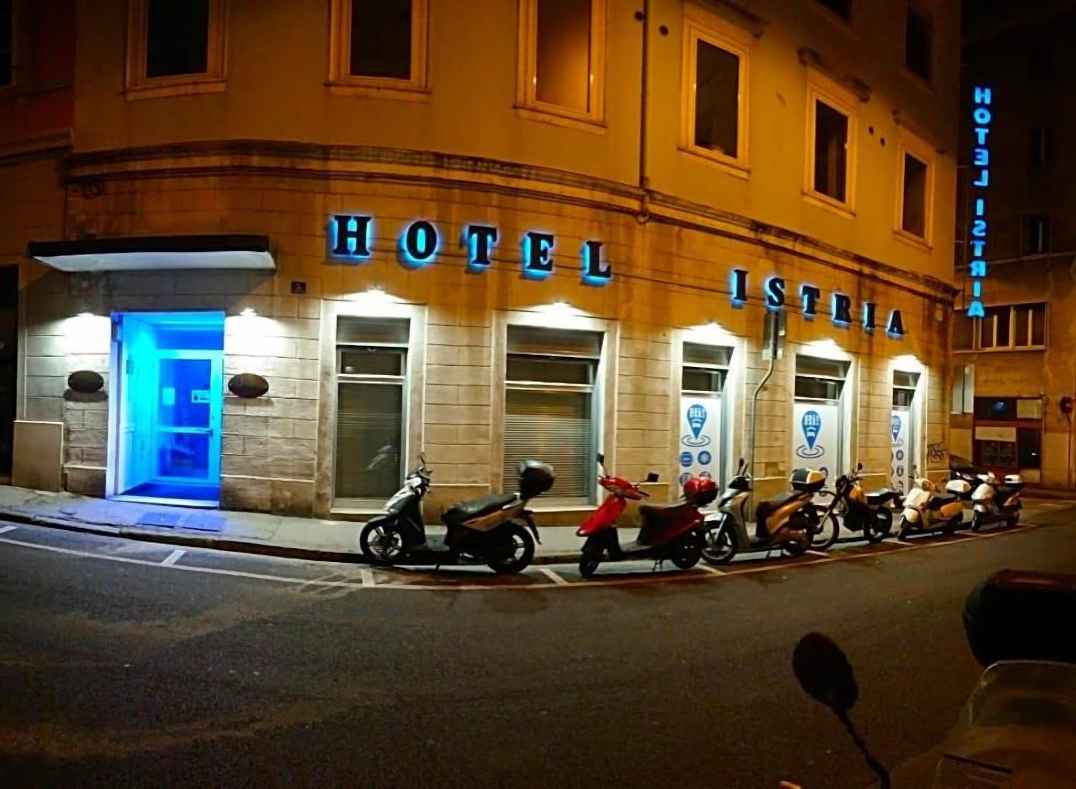 Un hotel con un letrero que dice 'HOTEL ISTORIA' y una fila de scooters estacionados al frente.