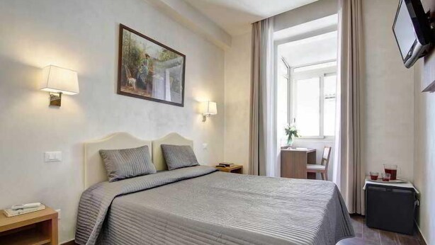 A hotel room with a bed, bedside tables, a television, and a window with curtains. - Romalive Hotel (Rome)