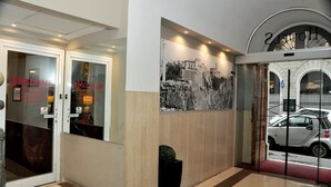 A hotel entrance with a reception desk, a large black and white photo on the wall, and a car parked outside. - Romalive Hotel (Rome)