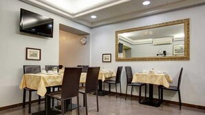A dining area with tables set for four, a flat-screen TV mounted on the wall, and a large mirror above the table. - Romalive Hotel (Rome)