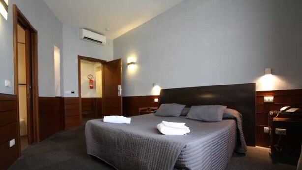 Habitación de hotel con una cama grande, mesitas de noche, un equipo de aire acondicionado y una puerta que da a otra habitación.