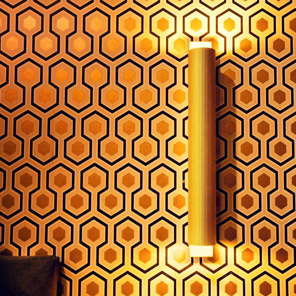 A wall with a geometric pattern of hexagons and a cylindrical object, possibly a lamp, on the right side.