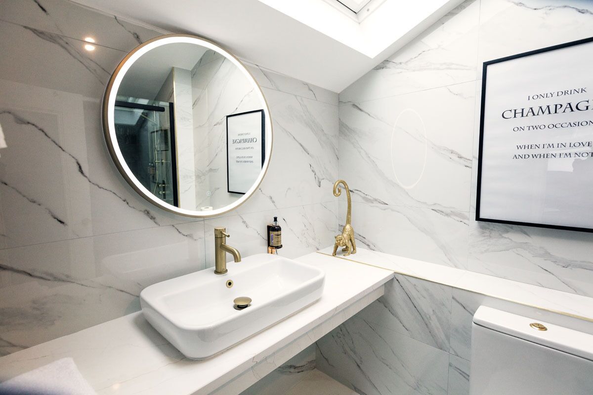 A modern bathroom with a white marble sink, gold fixtures, and a framed text on the wall.