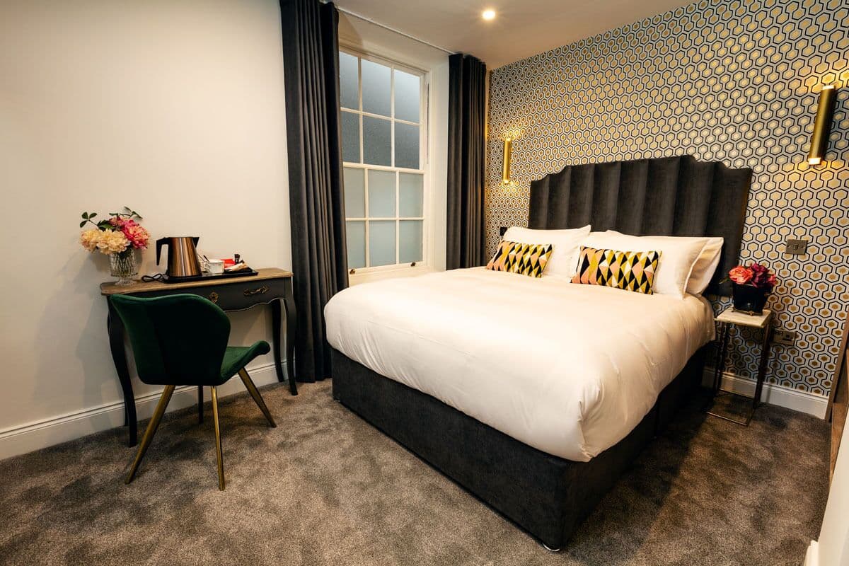 A hotel room with a large bed, a desk, a chair, and a nightstand.