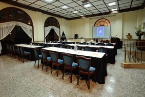 Un salón de conferencias con mesas largas, sillas, un atril y una pantalla.