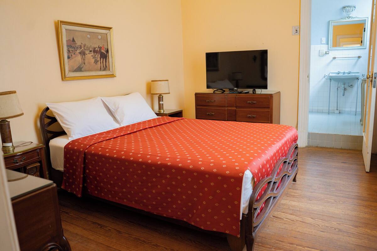 A hotel room with a bed, a television, a dresser, and a painting on the wall.