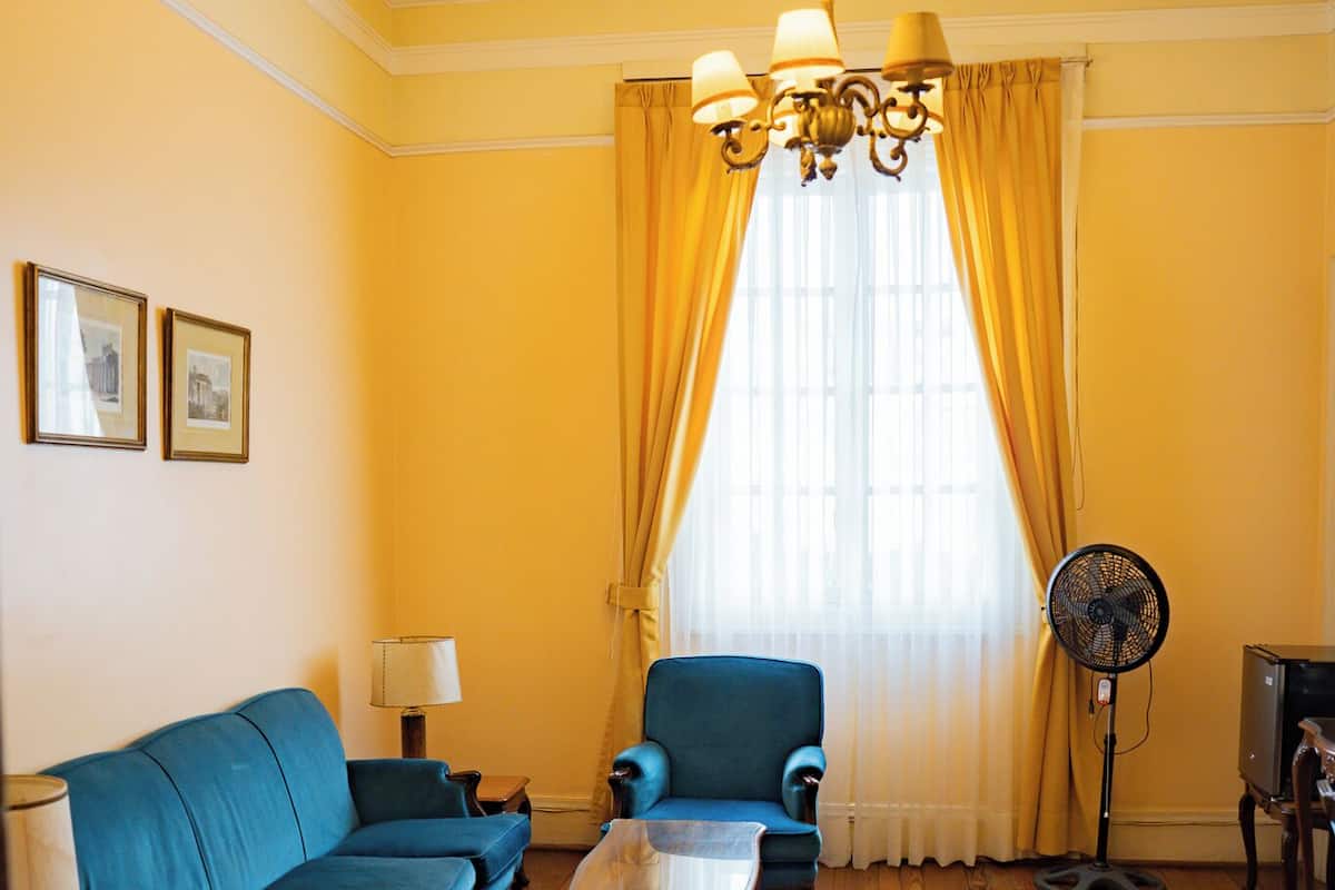 A room with a blue sofa, a wooden coffee table, a standing fan, and a television.