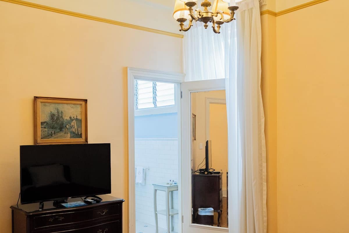 A room with a television on a dresser, a bed with a red cover, a chandelier, and a door leading to a balcony.
