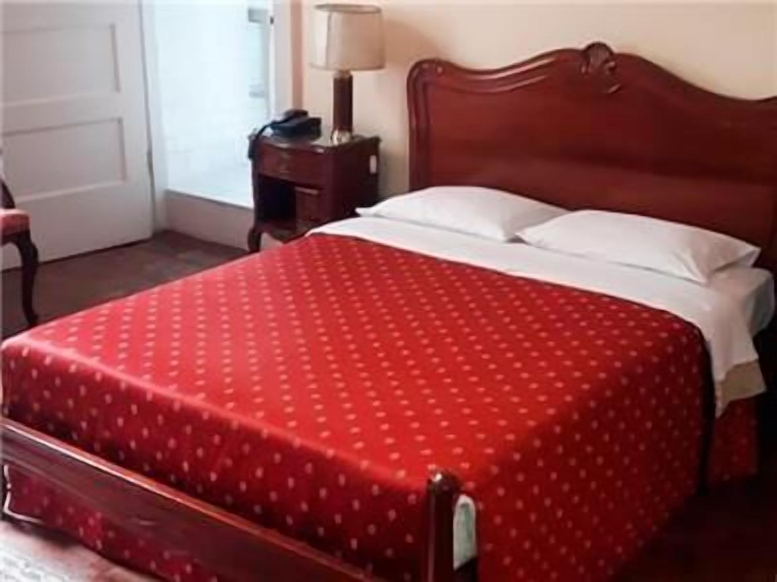 A bed with a red bedspread, a wooden headboard, and a nightstand with a lamp.