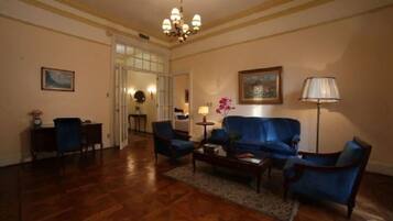 A room with a blue sofa, two armchairs, a coffee table, and a lamp. There is a door leading to another room.