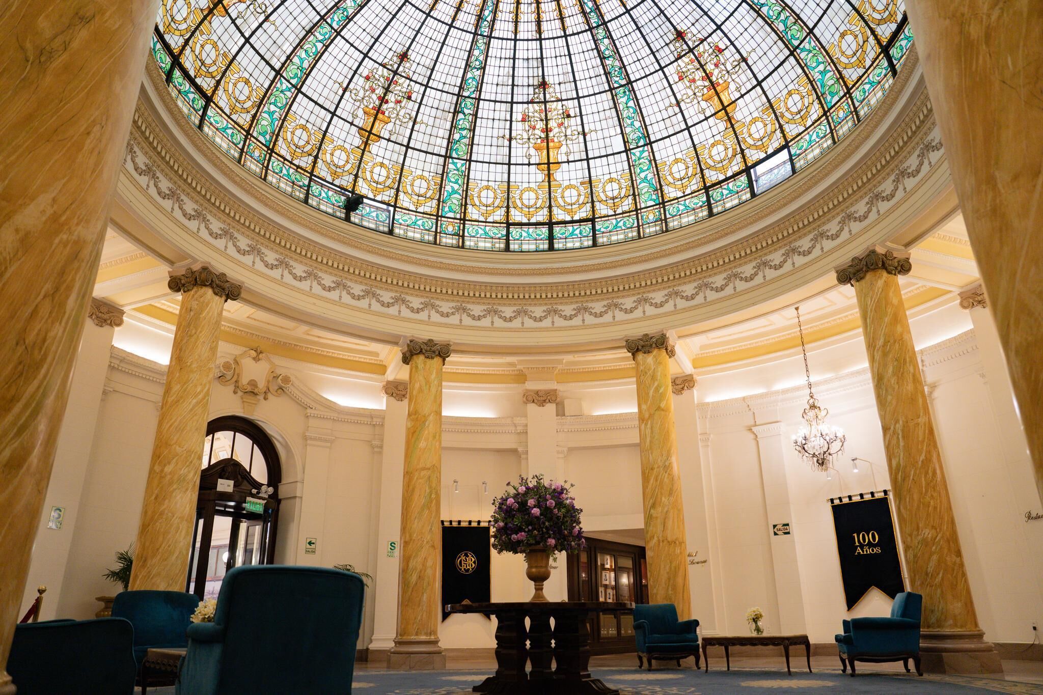 A grand lobby with a large stained glass dome, marble columns, and elegant seating.