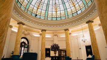 A grand lobby with a large stained glass dome, marble columns, and elegant seating.