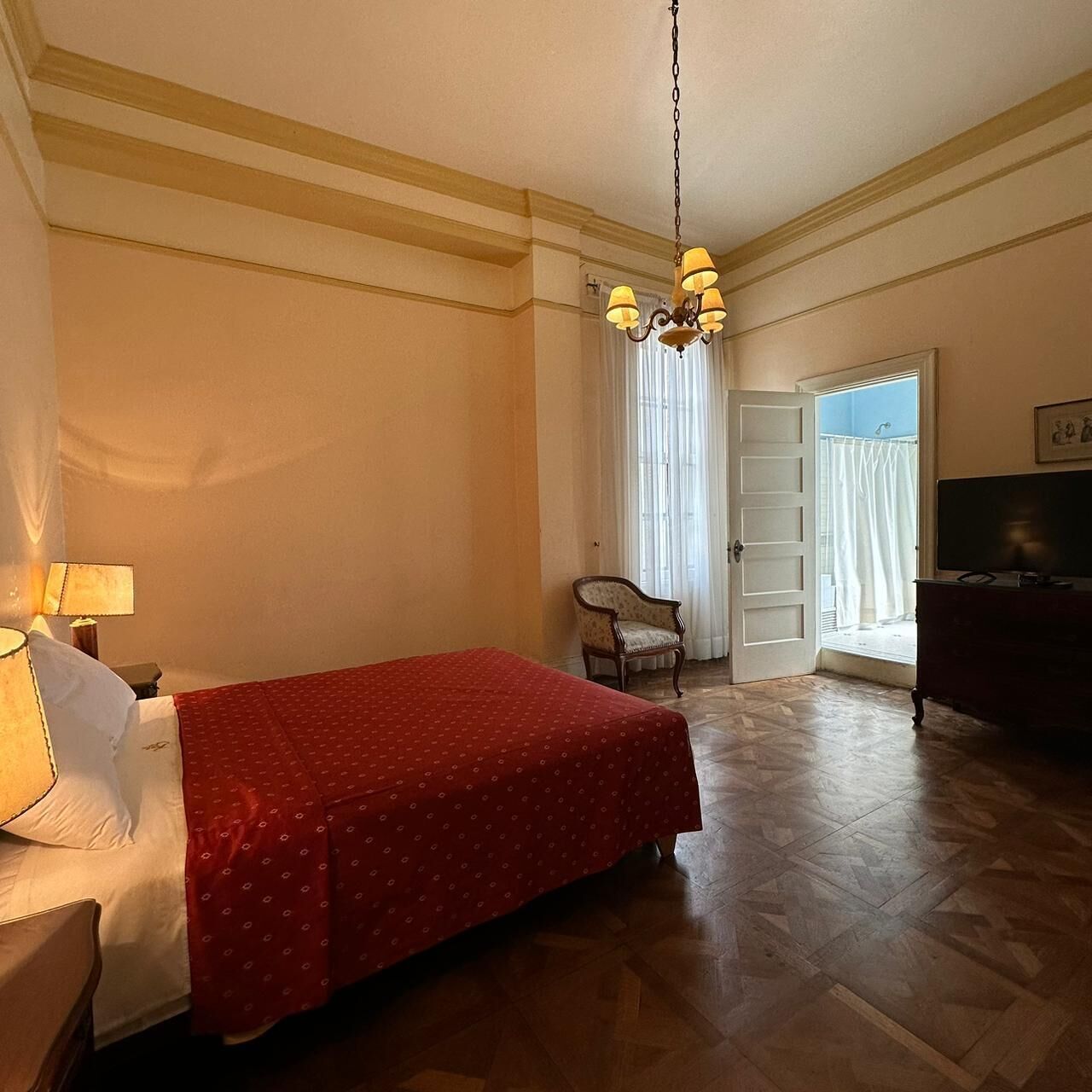 Una habitación de hotel con cama, una silla, televisor y candelabro.