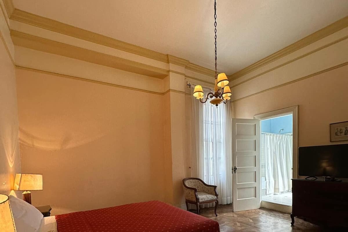 A hotel room with a bed, a chair, a television, and a chandelier.