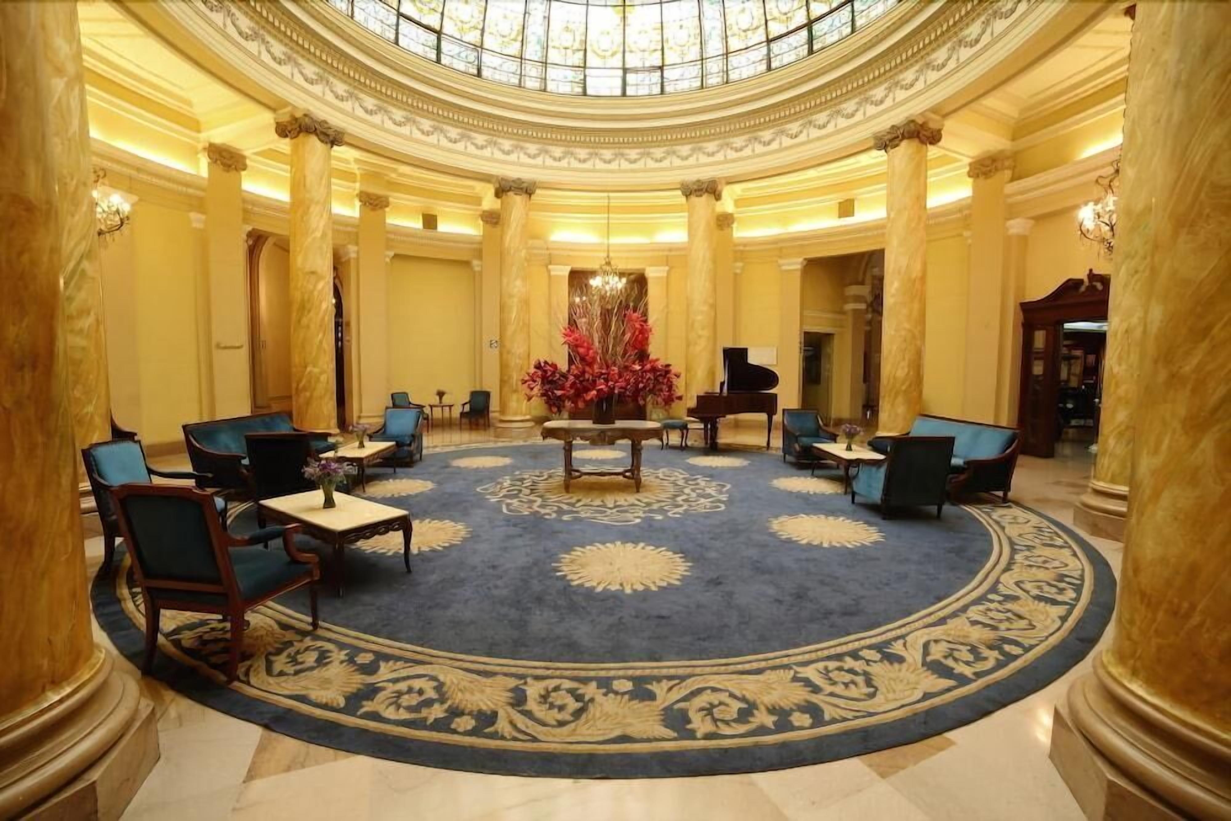 A grand lobby with a central chandelier, seating arrangements, and a patterned carpet.