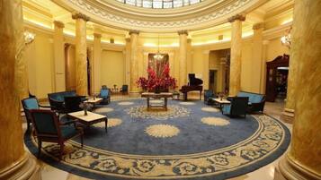 A grand lobby with a central chandelier, seating arrangements, and a patterned carpet.