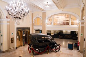 Un vestíbulo imponente con un coche clásico en exhibición, elegantes candelabros y una zona de recepción.