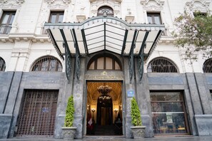 The entrance of Gran Hotel Bolivar with a classic architectural style, featuring a grand entrance, a chandelier, and two potted plants. - Gran Hotel Bolivar (Lima)