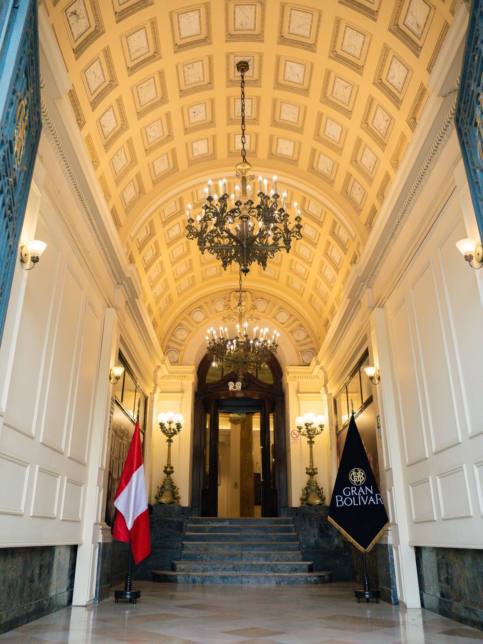 A grand hallway with a high ceiling, ornate chandeliers, and a flag.