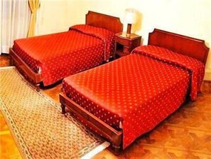 Una habitación con dos camas de madera, una mesita de noche con lámpara y una alfombra estampada.
