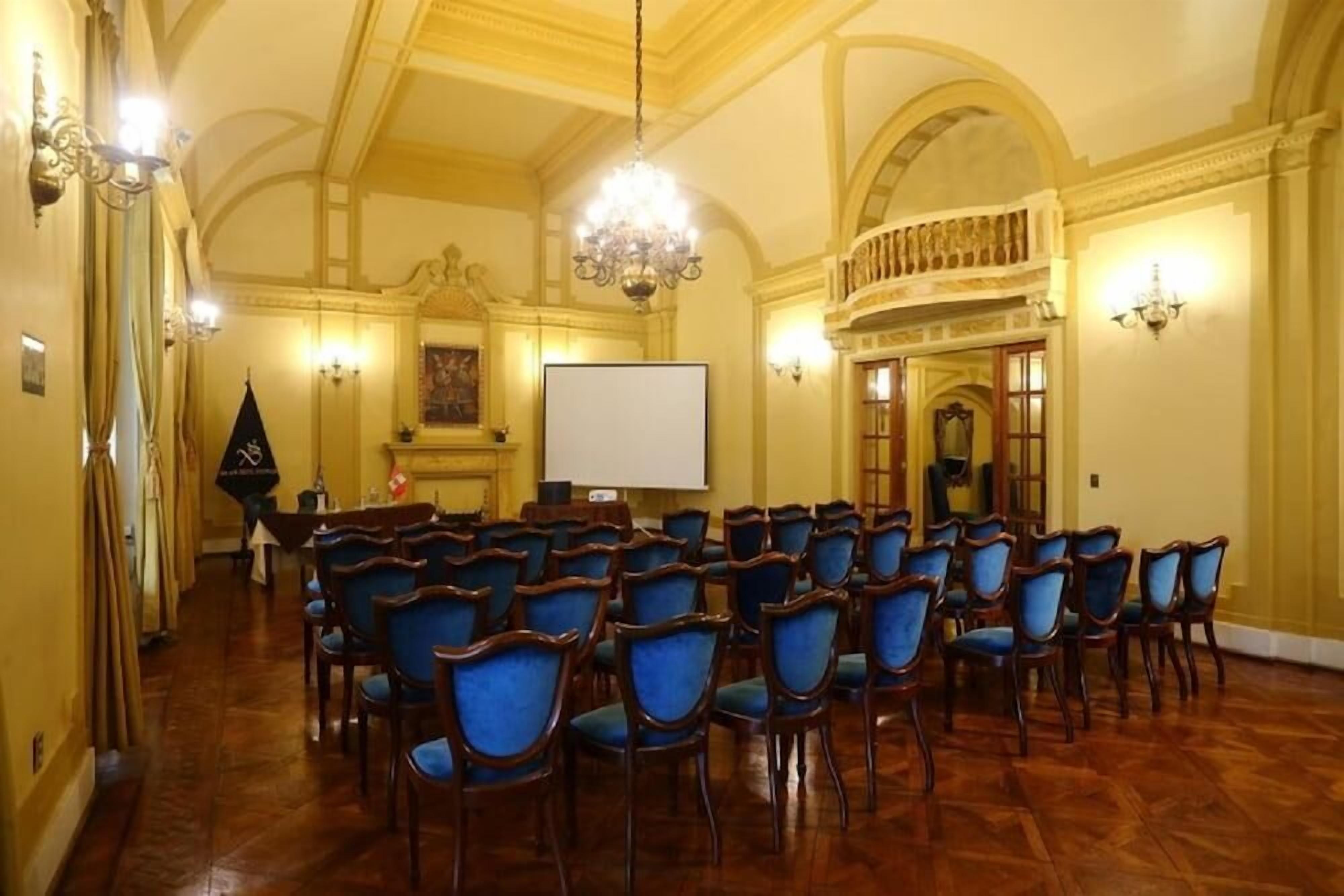 Una sala de conferències amb files de cadires, una pantalla de projector i un lampadari.