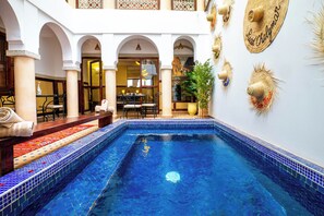 A pool area with a tiled edge, a seating area with chairs and a table, and decorative wall elements. - Riad Chalymar (Marrakech)