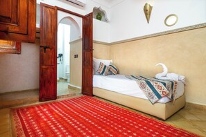 A bedroom with a bed, a red patterned rug, wooden doors, and a white wall with decorative elements.