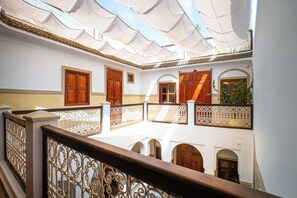 Une cour dotée d’une balustrade en bois, d’arcades et d’un plafond recouvert de carreaux.